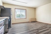 Located at 605 Chase Blvd in Sun Prairie, Wisconsin, this compact single-floor unit offers a practical and well-appointed layout comprising a kitchen and a full bathroom. Light-toned luxury vinyl plank flooring runs throughout the main living and kitchen areas, lending a clean, cohesive look to the space.

The kitchen is efficiently designed, featuring rich dark-stained wood cabinetry with ample upper and lower storage, a stainless steel sink with white countertops, a stainless steel range with an overhead ventilation hood, and a full-size stainless steel refrigerator. A stainless steel prep surface adds to the kitchen's utility. A wood-framed window allows natural light to fill the area, creating a bright and functional cooking environment.

The main open area provides versatile, open floor space with neutral cream-toned walls, wood baseboards, and a clean, minimalist finish. Exposed conduit runs along the ceiling, adding an industrial touch.

The bathroom is thoughtfully designed with accessibility in mind, featuring tile flooring, multiple stainless steel grab bars positioned near the toilet and along the walls, and a generous, open layout that accommodates mobility needs comfortably. Overall, this unit offers a straightforward, functional environment suited for a variety of uses.