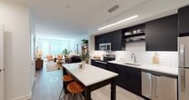 This thoughtfully designed single-floor residence combines modern aesthetics with comfortable living across an open, well-organized layout. The open-concept kitchen and living area serves as the heart of the home, where a striking kitchen outfitted with dark cabinetry, white subway tile backsplash, stainless steel appliances, and a white quartz island with bar seating flows seamlessly into the living space. A dedicated dining nook and built-in shelving add both functionality and character to the kitchen area. The living room is bright and inviting, featuring large windows that draw in generous natural light, light wood-tone flooring, and ample space for comfortable seating arrangements. Two bedrooms offer restful retreats, each with windows overlooking the exterior. The primary bedroom is distinguished by a bold botanical-print feature wall, plush carpeting, and room for a full suite of furniture. The second bedroom is bright and versatile, with neutral tones and a clean, airy feel. The bathroom presents a cohesive design with a floating dark vanity, large framed mirror, white quartz countertop, subway tile surround, and large-format tile flooring — completing this well-appointed residence.