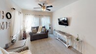This single-floor residence offers a thoughtfully designed layout that balances comfort and functionality throughout. The living room serves as the heart of the home, featuring plush carpeting, a ceiling fan with light fixture, and large windows dressed with sheer curtains that allow abundant natural light to fill the space. A wall-mounted flat-screen TV and a decorative console table complete the room's welcoming atmosphere.

The kitchen is equipped with warm-toned wood cabinetry, dark granite-style countertops, a double-basin sink, and white appliances including an electric range and built-in microwave. An L-shaped peninsula with bar seating provides a casual dining option and opens to the entryway with hardwood-style flooring. Adjacent to the kitchen, a dedicated dining area features a sliding glass door offering outdoor views, complemented by vertical blinds and a decorative wall mirror.

A carpeted hallway connects the private quarters, which include multiple bedrooms. Each bedroom features ceiling fans, generous natural light from large windows, and soft carpet underfoot. One bedroom benefits from dual windows and ample space for furniture. A built-in desk area in the hallway provides a convenient workspace.

The full bathroom includes a vanity with granite-style countertops, a lighted mirror, a tub-shower combination, and direct access to a spacious walk-in closet, rounding out this well-equipped residence.