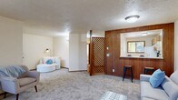Located at 1884 Happy Ln in Eugene, Oregon, this single-floor, 2-bedroom, 1-bathroom home blends mid-century character with practical everyday living. The living area is a defining feature of the home, offering generous open space with soft carpet underfoot, a textured ceiling, and a distinctive warm-toned wood lattice partition that adds architectural charm while naturally delineating zones within the space. Large windows invite natural light and frame views of surrounding greenery, enhancing the overall ambiance. A pass-through opening connects the living space to the kitchen, which is equipped with warm oak cabinetry, white appliances including a range, dishwasher, and refrigerator, tile flooring, and a window overlooking the outdoors. A louvered pantry door adds a classic touch. The full bathroom features a tub-shower combination and tile flooring. Both bedrooms are carpeted and well-proportioned, with the primary bedroom offering a walk-in closet alongside additional louvered bifold closet doors, providing ample storage. Warm wood trim and doors are consistent throughout, lending a cohesive, welcoming feel. A dedicated laundry room adds everyday convenience, rounding out this well-appointed Eugene home.