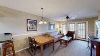 Located in Clarkesville, Georgia, this well-appointed 2-bedroom, 3-bathroom unit offers a thoughtfully designed single-floor layout that maximizes comfort and functionality. The living room serves as a welcoming gathering space, featuring plush seating, a ceiling fan, framed local artwork, and French doors fitted with wood blinds that allow natural light to filter in while maintaining privacy. The fully equipped kitchen includes white cabinetry with beadboard detailing, dark countertops, a full suite of appliances, a stainless steel sink, and tile flooring — providing everything needed for home-style cooking. The primary bedroom is a spacious retreat furnished with a king-sized bed, a wooden headboard, a ceiling fan, and a bench at the foot of the bed, complemented by a window overlooking the surrounding greenery. The en-suite primary bathroom features a soaking jetted tub with a shower curtain, white beadboard cabinetry, and stone-look tile flooring. The second bedroom offers a similarly comfortable setup with a ceiling fan, natural light from dual windows, and a vanity with a mirror. Additional bathrooms include a full tub-shower combo with a vanity and tile flooring. Throughout the space, warm neutral tones, carpeted bedrooms, and consistent cottage-style finishes create a cohesive and relaxing ambiance.