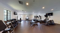 Located at 1300 Southampton Rd in Benicia, CA, this well-equipped fitness center offers a comprehensive workout environment within a single-floor layout. The space is designed with functionality and comfort in mind, featuring durable rubber flooring throughout that provides both safety and stability during exercise.

The cardio zone is prominently featured, housing multiple Life Fitness treadmills and elliptical cross-trainers arranged to allow ample space between each machine. Wall-mounted flat-screen TVs are positioned throughout the room, enabling users to stay entertained during their workouts. A dedicated area for strength training includes a multi-function cable and weight machine, a Life Fitness adjustable resistance machine, and a flat weight bench, catering to a range of strength-focused routines.

The free weight section lines one wall with a full rack of dumbbells, complemented by a weight bench for versatile lifting options. A large floor-to-ceiling mirror on one wall enhances the sense of space and allows users to monitor their form. Indoor cycling bikes add yet another cardio option to the facility's diverse offerings.

Natural light filters in through multiple windows with black-framed trim, giving the space an open and inviting atmosphere. Recessed ceiling lighting ensures the room is well-lit at all times. Multiple entry points, including glass-paneled doors leading to the outdoors, contribute to the airy feel of this thoughtfully appointed fitness facility.