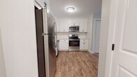 Located at 969 Hopmeadow St in Simsbury, Connecticut, this single-floor unit has been thoughtfully updated with a clean, modern aesthetic that carries consistently throughout every room. The kitchen serves as a standout feature, equipped with a full suite of stainless steel appliances — including a refrigerator, range, over-the-range microwave, and dishwasher — paired with crisp white shaker-style cabinetry, a white tile subway backsplash, and light countertops. Warm wood-look luxury flooring flows seamlessly through the kitchen and into the adjacent living and dining areas, creating a cohesive and inviting atmosphere. An open transition between the kitchen and the living space allows for a flexible, functional layout with a dedicated pantry closet nearby for additional storage. The living areas are bright and airy, with natural light entering through windows that frame views of surrounding trees, lending a tranquil, nature-connected feel. The bedroom offers a comfortable, well-proportioned space with a window view and a wall-mounted heating unit. The bathroom is neatly appointed with a dark-finish vanity, white countertop, framed mirror, and updated fixtures against clean white walls and matching wood-look flooring. Overall, this unit presents a well-maintained, move-in-ready space with modern finishes in a serene Simsbury setting.