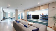 Located at 47 William Howard Taft Rd in Cincinnati, Ohio, this single-floor space offers a thoughtfully designed open-plan layout that blends functionality with modern aesthetics. The interior is defined by polished concrete floors, exposed structural columns, and clean white ceilings with recessed lighting, creating a bright and airy atmosphere throughout.

The lounge area anchors one end of the space, centered around a large modular sectional sofa in neutral gray, accented with vivid cobalt blue throw pillows. A custom built-in entertainment wall features a wall-mounted flat-screen TV, vibrant blue display shelves, and lower cabinetry — all framed by warm wood upper cabinets with bold red trim accents that carry throughout the space as a unifying design element.

Floor-to-ceiling black-framed glass partitions divide the lounge from a collaborative work and dining zone, which includes a substantial communal table with modern seating. This transparent division maintains visual connectivity while providing acoustic separation.

The kitchenette is a standout feature, showcasing teal cabinetry, white subway tile backsplash, a matte black sink, and ample upper storage. Its crisp, color-forward design continues the space's energetic palette. Natural light filters in through exterior windows along the perimeter, complementing the recessed lighting to keep the environment welcoming and well-illuminated throughout the day.
