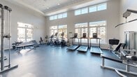 Located at 2000 Brandt Dr in Cranberry Township, PA, this well-appointed fitness center delivers a comprehensive workout environment designed for both cardio and strength training. The facility is spread across a single floor and is divided into distinct functional zones, each thoughtfully equipped for a range of exercise disciplines.

The cardio area is immediately striking, featuring soaring ceilings and an expansive wall of floor-to-ceiling windows that flood the space with natural light and offer open views of the surrounding community. Multiple treadmills, ellipticals, and stationary bikes are arranged to take full advantage of the bright, airy atmosphere, giving users an energizing environment for their workouts.

A dedicated strength training zone houses a robust selection of resistance machines, cable systems, free-weight benches, and a power rack, all by Matrix. Plyometric boxes and stability balls round out the functional fitness offerings. This area also benefits from elevated ceilings that contribute to a spacious, unconfined feel.

Throughout the facility, durable rubber flooring in both blue and grey tones provides safety and comfort underfoot. Clean white walls and recessed lighting maintain a modern, professional aesthetic. The overall ambiance is bright, open, and motivating — a well-designed space suited to support a wide variety of fitness goals.