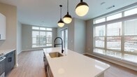 Located at 600 Willard St in Durham, NC, this single-floor residence showcases a clean, contemporary design with an open-concept layout that seamlessly connects the kitchen and living areas. The kitchen is a standout feature, anchored by a large island with a white quartz countertop, an undermount sink, and a matte black pull-down faucet. Sleek white high-gloss cabinetry, subway tile backsplash, stainless steel appliances, and a trio of globe pendant lights complete the space. Light wood-look flooring runs throughout the main living areas, while large windows with horizontal blinds invite ample natural light and views of the surrounding Durham cityscape. A dedicated mudroom/entry nook offers built-in shelving, hooks, and a bench for added functionality. The bedrooms feature plush carpet, ceiling fans, and generously sized windows. The bathroom is well-appointed with a dual-sink vanity featuring white cabinetry and quartz countertops, matte black fixtures, a large mirror, tile flooring, and a glass-enclosed walk-in shower. Neutral wall tones and consistent modern hardware tie the aesthetic together throughout the entire residence.