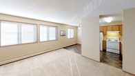 This single-floor unit offers a practical and well-organized layout designed for comfortable everyday living. The open living area is generously sized, featuring neutral beige walls, soft wall-to-wall carpeting, and a textured ceiling. Multiple windows along one wall allow natural light to fill the space, while a wall-mounted air conditioning unit and baseboard heating provide year-round climate control. A ceiling fan is positioned at the transition point between the living area and the kitchen.

The kitchen is efficiently arranged with warm oak cabinetry spanning both upper and lower sections, a double-basin sink, a full-size refrigerator, dishwasher, and a tile floor in a dark stone pattern. Fluorescent overhead lighting ensures the kitchen is well-lit.

The bedroom is carpeted and includes a window with natural light and a closet with wood-panel doors. A hallway connects the bedroom to additional storage and the full bathroom, which features a single-sink vanity with oak cabinet storage, a wall mirror with bar lighting, a soaker tub with grab bars, and tile flooring. The entry area includes a closet and transitions smoothly into the main living space.
