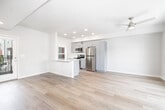 This thoughtfully designed one-bedroom, one-bathroom unit offers an efficient and modern single-floor layout. The open-concept kitchen and living area serves as the heart of the space, featuring light hardwood flooring throughout and a ceiling fan that enhances airflow and comfort. The kitchen is well-appointed with gray shaker-style cabinetry, stainless steel appliances including a refrigerator, electric range, and built-in microwave, as well as a peninsula with a white quartz countertop and an undermount sink — ideal for both meal preparation and casual dining. A window and exterior door access provide natural light and outdoor connectivity to this main living area. The bedroom is a comfortable, carpeted retreat with multiple windows that invite natural light and offer neighborhood views, along with a closet for storage. A second area with hardwood flooring and a ceiling fan provides additional flexible living space with a large picture window framing outdoor greenery. The bathroom is clean and modern, featuring a white vanity with quartz countertop, an undermount sink, wood-look tile flooring, and a window for natural light. Throughout the unit, a neutral color palette and contemporary finishes create a cohesive, move-in-ready environment.