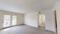 This one-bedroom, one-bathroom single-story unit in Elizabethtown, Kentucky offers a practical and comfortable layout across a well-utilized floor plan. The living room serves as the heart of the home, featuring plush carpet flooring, neutral cream-toned walls, and a pair of French doors that flood the space with natural light and offer views of the surrounding greenery. A ceiling fan overhead adds comfort to the open atmosphere. The kitchen is thoughtfully designed with warm wood cabinetry, dark countertops, light hardwood-style flooring, and black appliances including a range, microwave, and dishwasher, providing ample storage and workspace. The generously sized bedroom features soft carpet, natural light from a window, and the convenience of two closets, offering notable storage capacity. The full bathroom includes a tub-shower combination, toilet, and a wood-toned vanity with countertop storage, all finished with hardwood-style flooring. A dedicated laundry room with hookups and overhead wire shelving adds everyday convenience. A hallway connects the rooms efficiently, completing this well-organized, move-in-ready unit.