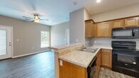 This single-story residence offers a well-designed layout with a consistent neutral color palette and durable finishes throughout. The kitchen serves as a central highlight, featuring warm honey-toned cabinetry with raised panel doors, light granite-look countertops, and a peninsula that opens toward the living area, creating a naturally connected, open-concept flow. Black Whirlpool appliances, including a refrigerator, range, microwave, and dishwasher, provide a cohesive and functional cooking space. Wood-look plank flooring extends through the kitchen, living, and entry areas, offering a clean, modern aesthetic.

The living area is generously proportioned, with neutral gray walls, a ceiling fan, and natural light from a window overlooking the outdoors. The entry area features a paneled front door and direct access to adjacent rooms. Bedrooms are finished with plush carpet flooring, ceiling fans, and windows that bring in natural light and outdoor views, contributing to a comfortable atmosphere. The bathroom includes a full tub-shower combination with a curved curtain rod, wood-look vinyl flooring, and clean white fixtures, maintaining the home's consistent, practical design throughout.