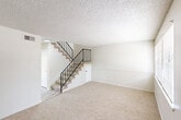 Located at 865 S Flannery Rd in Baton Rouge, Louisiana, this two-story, two-bedroom, two-bathroom home offers a practical and comfortable layout across two floors. The ground floor houses the main living area and kitchen. The living room features neutral-toned carpet, a textured ceiling, and a large window that invites natural light into the space. A staircase with a sleek black metal railing connects the floors, adding a functional focal point to the main level. The galley-style kitchen is equipped with white cabinetry, laminate countertops, wood-look flooring, and white appliances including a range and refrigerator, making efficient use of the available space. A dedicated laundry area with a full-size washer and dryer provides added in-unit convenience. Upstairs, both bedrooms are carpeted and feature textured ceilings, ceiling fans with integrated light fixtures, and windows that allow for natural light. The spacious primary bedroom offers a generous footprint with ample room for furnishings. The two bathrooms are clean and functional, with mirrored accents. Throughout the home, a neutral color palette of whites and warm beiges creates a bright, cohesive atmosphere well-suited for comfortable everyday living.