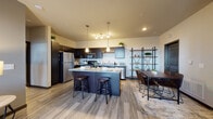 This thoughtfully designed single-floor residence offers a seamless blend of modern aesthetics and functional living. The open-concept kitchen serves as the heart of the space, showcasing dark espresso cabinetry, granite countertops, and a full suite of stainless steel appliances. A central island with bar seating provides additional prep space and casual dining options, while pendant lighting above adds a warm, focused ambiance. The kitchen flows naturally into a dedicated dining area, complete with an industrial-style shelving unit that adds character and storage.

The living room is bright and welcoming, featuring large windows that allow generous natural light to fill the space. Neutral-toned walls complemented by a rich charcoal accent wall create a contemporary, polished atmosphere ideal for relaxing or entertaining.

The bedrooms offer a calm retreat, each carpeted for comfort and equipped with large windows framing outdoor views. The rooms provide ample space for furnishings and are finished with clean, neutral tones.

The bathroom is functional and neatly appointed, featuring a full tub-shower combination, wood-look flooring, granite-topped vanity, and dark cabinetry that ties cohesively into the overall design language of the unit. Wood-look flooring runs throughout the main living areas, unifying the space with a warm, contemporary feel.