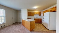 Located at 406 Sanford St in Radford, Virginia, this single-floor unit offers a practical and well-organized layout designed for comfortable everyday living. The kitchen serves as a central feature of the space, outfitted with warm oak cabinetry, light countertops, and a full suite of white appliances including an electric range, dishwasher, microwave, and refrigerator. A peninsula counter extends into the living area, creating a natural division between the kitchen and the carpeted living space while offering additional prep and seating space. The kitchen floor is finished with durable tile, providing a clean contrast to the soft carpeting found throughout the living and bedroom areas. The bedroom is generously proportioned, featuring plush carpeting and a neutral color palette that allows for flexible furnishing arrangements. The bathroom includes an oak vanity with a white countertop, a well-lit mirror above, and tile flooring consistent with the rest of the wet areas. A dedicated laundry area houses a stacked washer and dryer unit alongside built-in wire shelving, adding valuable storage and in-unit convenience. The overall design throughout is clean and functional, with white walls and consistent finishes that create a cohesive, move-in ready environment.