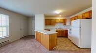 Located at 406 Sanford St in Radford, Virginia, this single-floor unit offers a practical and well-organized layout designed for comfortable everyday living. The kitchen serves as a central feature of the space, outfitted with warm oak cabinetry, light countertops, and a full suite of white appliances including an electric range, dishwasher, microwave, and refrigerator. A peninsula counter extends into the living area, creating a natural division between the kitchen and the carpeted living space while offering additional prep and seating space. The kitchen floor is finished with durable tile, providing a clean contrast to the soft carpeting found throughout the living and bedroom areas. The bedroom is generously proportioned, featuring plush carpeting and a neutral color palette that allows for flexible furnishing arrangements. The bathroom includes an oak vanity with a white countertop, a well-lit mirror above, and tile flooring consistent with the rest of the wet areas. A dedicated laundry area houses a stacked washer and dryer unit alongside built-in wire shelving, adding valuable storage and in-unit convenience. The overall design throughout is clean and functional, with white walls and consistent finishes that create a cohesive, move-in ready environment.