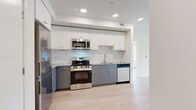 This contemporary 1-bedroom apartment in Kelowna offers a well-designed living space of 50 square meters. The heart of the home is a modern kitchen, showcasing a two-tone color scheme with white upper cabinets and contrasting gray lower units. Stainless steel appliances, including a refrigerator, stove, microwave, and dishwasher, complement the sleek design. A striking marble-patterned backsplash adds a touch of luxury.

The living area is bathed in natural light from large windows, offering views of the surrounding area. Light wood flooring throughout creates a sense of warmth and continuity. The bedroom, measuring 10 square meters, continues the bright and airy feel with multiple windows.

Storage is thoughtfully incorporated, with a dedicated closet space featuring wire shelving. The bathroom is pristine, with a white color palette and a combined tub and shower unit. The overall design emphasizes clean lines and a minimalist aesthetic, making efficient use of the compact space. An outdoor area, likely a balcony or patio, is accessible, extending the living space. Located at 500 Asher Rd in Kelowna, this apartment offers modern living in a concise, well-planned layout.
