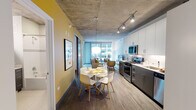 Located in Chicago's vibrant Loop neighborhood at 56 E Randolph St, this single-floor unit showcases a contemporary urban design defined by striking exposed concrete ceilings throughout. The open-concept living, dining, and kitchen area is anchored by floor-to-ceiling windows that flood the space with natural light and offer views of the surrounding cityscape.

The kitchen is well-appointed with stainless steel appliances, including a gas range, microwave, dishwasher, and refrigerator. Two-tone cabinetry pairs white upper cabinets with charcoal lower units, complemented by light countertops and a subway tile backsplash. A stacked in-unit washer and dryer is conveniently tucked away nearby.

The dining area accommodates a round table with seating for four, while the living room provides comfortable space for lounging with direct access to natural light from the expansive window wall. Wood-style flooring runs throughout the main living areas, adding warmth against the industrial ceiling.

The bedroom features exposed concrete ceilings, dark hardwood floors, and a spacious walk-in closet with built-in shelving and a full-length hanging rod. The bathroom includes a dark-vanity with a mirrored medicine cabinet and a tiled soaking tub and shower combination.