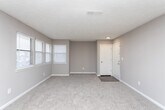 This single-floor residence at 518 Monterey Pkwy in Sandy Springs, Georgia offers a practical and well-organized layout with a neutral color palette of warm taupe tones throughout. The open-concept living area is carpeted and features a ceiling fan with light fixture, a floor vent for climate control, and sliding vertical blinds that lead to an outdoor access point. The space flows seamlessly into the kitchen, which is set apart by wood-look vinyl flooring. The kitchen is equipped with white cabinetry, light stone-look countertops, a peninsula with a sink, black appliances including a refrigerator and gas range, and a ventilation hood. Overhead fluorescent lighting and a window provide functional illumination. The bedrooms are carpeted and finished with the same neutral tones, each offering natural light through blinds-covered windows. One bedroom features vaulted ceilings that add a sense of openness, while another includes a built-in closet with shelving. The bathrooms include one with a white vanity, stone-look countertop, large mirror, and wood-look flooring, and a second with a tiled tub-shower combination. Textured ceilings are present throughout the unit.