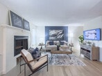 Located at 3200 Oakwood Village Lane in Atlanta, Georgia, this single-floor residence offers a well-appointed and cohesive living environment with a contemporary design aesthetic. The living room serves as the heart of the home, anchored by a classic white-mantel fireplace and enhanced by a striking navy blue accent wall adorned with bold artwork. Light wood-style flooring runs throughout, adding warmth and continuity across the space. The living area flows seamlessly into the dining area, which benefits from natural light streaming through sliding glass doors with vertical blinds and is finished with a ceiling fan overhead. The kitchen features white raised-panel cabinetry, granite-look countertops, and stainless steel appliances including a range, over-the-range microwave, and refrigerator, all complemented by a window that brings in additional natural light. The primary bedroom showcases a deep navy accent wall paired with large-scale artwork, creating a bold and restful retreat. A second bedroom carries a softer blue-gray accent wall with coordinating framed art and warm metallic wall décor, offering a calm and inviting atmosphere. Textured ceilings are consistent throughout the home. The overall design blends modern furnishings with rich color accents, resulting in a stylish and comfortable living space.