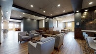 Located at 50 Public Square in the heart of Cleveland, Ohio, this single-floor amenity space offers a well-appointed and thoughtfully designed environment suited for both social gatherings and relaxed downtime. The open lounge area serves as the central hub, furnished with contemporary upholstered sofas and armchairs arranged around wooden coffee tables, all set atop warm hardwood flooring. Recessed lighting and a dark tiled ceiling give the space a refined, modern ambiance, while a wall-mounted flat-screen television adds a functional touch. Adjacent to the lounge, a fully equipped kitchen stands out with rich dark walnut cabinetry, striking herringbone-patterned tile backsplashes, stone countertops, a double wall oven, a large island, and pendant lighting — delivering both elegance and practicality. Intimate booth seating alcoves, finished in leather banquettes and accompanied by small bistro tables with vibrant accent chairs, provide semi-private nooks ideal for conversation. A dedicated game room, filled with natural light from multiple windows, houses shuffleboard and billiards tables atop dark hardwood floors, offering an engaging recreational retreat. Open transitional corridors connect each zone, maintaining a cohesive flow throughout the entire space.