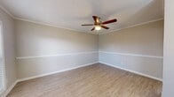 This single-floor residence presents a thoughtfully designed layout with a cohesive aesthetic throughout. The living areas are finished with light-toned wood laminate flooring that extends seamlessly across the main spaces, complemented by crisp white baseboards and elegant crown molding that frames each room with a refined touch. Ceiling fans are present in multiple rooms, providing both practical ventilation and a subtle decorative element.

The open entry and dining area is anchored by a stylish chandelier, creating a welcoming focal point as you enter the home. The adjacent kitchen is efficiently arranged and features black appliances — including a refrigerator, electric range, and over-the-range microwave — set against light gray cabinetry and marble-look countertops, with a clean tile backsplash adding visual interest.

The bedrooms offer a comfortable contrast with soft, neutral-toned carpeting underfoot and ceiling fans overhead. Crown molding continues into these spaces, maintaining design consistency throughout the home. Natural light filters in through windows dressed with blinds, enhancing the bright, airy atmosphere.

Overall, the space presents a clean, move-in-ready environment with neutral tones, durable finishes, and functional details that cater well to everyday living.