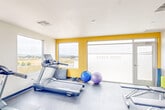 The Parke West Fitness Center at 1060 Village Dr in Santa Maria, California, is a thoughtfully designed community gym offering a comprehensive workout environment within a single open floor. The space features a clean, modern aesthetic with white walls accented by bold yellow panels that add a vibrant energy to the room. Large picture windows line multiple walls, flooding the interior with natural light and providing sweeping views of the surrounding Santa Maria landscape, including rolling hills and open fields.

The fitness floor is covered in durable rubber flooring and is well-organized to accommodate a full range of exercise options. Cardio equipment includes multiple Spirit treadmills, a stationary bike, and an elliptical machine, all positioned to take advantage of the scenic outdoor views. Strength training is supported by a multi-station cable machine, a dumbbell rack with free weights, and a weight bench. Additional workout accessories such as exercise balls, resistance equipment, and yoga/stretching mats are neatly stored and accessible. A wall-mounted flat-screen television is available for entertainment during workouts. A full-length mirror enhances the sense of openness, while the Parke West branding is prominently displayed on frosted glass near the entrance, reinforcing the facility's community identity.