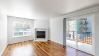 Located at 602 Galer Street in Seattle's Queen Anne neighborhood, this single-floor residence offers a thoughtfully designed layout with a clean, modern aesthetic throughout. The living area is a standout, featuring rich hardwood flooring, crisp white walls, and a classic fireplace with a simple tile surround. Natural light fills the space through multiple windows with blinds, and a sliding glass door opens directly onto a private balcony, providing views of the surrounding neighborhood. The kitchen is efficiently arranged in a galley style, showcasing navy lower cabinets paired with white uppers, light countertops, a tile backsplash, stainless steel appliances including a refrigerator and range, and an in-unit washer and dryer conveniently tucked nearby. A peninsula with a pendant light connects the kitchen to the main living area. The bedrooms feature plush carpeting, soft neutral tones, and windows that bring in natural light; one bedroom also includes baseboard heating. Two bathrooms serve the unit — one with a tub/shower combination and a navy vanity, and another with a sleek glass-enclosed shower. A carpeted hallway with accent walls in a soothing teal hue connects the private areas of the home, adding a subtle touch of character to the overall design.