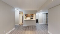 Located at 2117 Woodburn Dr SE in Grand Rapids, Michigan, this one-bedroom, one-bathroom unit offers a well-designed, efficient layout across a single floor. Light gray luxury vinyl plank flooring flows throughout the main living areas, creating a clean and cohesive aesthetic.

The combined kitchen and living room forms the heart of the unit. The kitchen features warm-toned cabinetry, a classic white subway tile backsplash, stainless steel appliances including a refrigerator, range, and over-the-range microwave, and a curved white peninsula with a double-basin sink — ideal for both prep and casual dining. The open layout allows the kitchen to connect seamlessly to the living area, which benefits from natural light and a ceiling fan.

The bedroom is carpeted for comfort and includes a ceiling fan, a window with outdoor greenery views, and a sliding glass door that opens to a private balcony. A dedicated laundry area houses a stacked Whirlpool washer and dryer unit alongside built-in shelving, adding practical convenience.

The bathroom is finished with wood-toned cabinetry, a quartz-style countertop, light vinyl flooring, and a full tub-shower combination with a curved curtain rod. Neutral warm-beige tones throughout the unit create a calm, move-in-ready atmosphere.