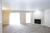 This single-story home presents a practical and well-organized layout across its living spaces. The living room serves as a central gathering area, featuring a tile-surround fireplace, plush wall-to-wall carpeting, and a sliding glass door alongside an additional window that brings in natural light and provides outdoor views. A textured ceiling runs throughout the common areas, adding a classic residential character.

The kitchen is accessible via an open pass-through counter that connects it to the main living area, creating a semi-open feel. It is equipped with wood-toned cabinetry, white countertops, black appliances including a refrigerator and dishwasher, and durable tile flooring. A louvered door adds a charming detail to the space.

The bedrooms are carpeted and well-proportioned, each receiving natural light through sizable windows with blinds. One bedroom includes a ceiling fan, while another features two doorways leading to a walk-in closet and an additional room or hallway. A dedicated vanity area with a floating wood-accented countertop and a lighted mirror connects to a private toilet room, offering a functional ensuite arrangement. A full bathroom with a tub-shower combo, sliding glass enclosure, tile floors, and a wood-cabinet vanity serves the remaining rooms.