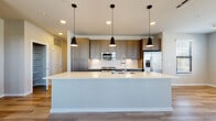 Located on Foxtail Palm Way in Bradenton, Florida, this single-story home showcases a clean, contemporary design with consistent finishes throughout. The kitchen serves as a central highlight, featuring a large island with a bright white quartz countertop, an integrated sink, and three sleek pendant lights overhead. Warm-toned flat-front cabinetry lines the walls alongside a white subway tile backsplash, stainless steel appliances—including a French door refrigerator, range, and built-in microwave—and light hardwood-style flooring that extends into the surrounding areas.

The bedrooms offer plush carpeting underfoot, ceiling fans, and windows with horizontal blinds that allow natural light to filter in. Each bedroom includes closet space with built-in shelving, providing practical storage. The bathrooms are finished with wood-grain cabinetry, white countertops, and light plank flooring. One bathroom features a walk-in shower enclosed by a glass door and framed with white vertical tile. A dedicated laundry area with a washer and overhead shelving adds everyday convenience. The overall layout, as seen in the 3D model, presents a well-organized, open-feeling floor plan suited for comfortable single-level living.