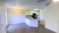 This two-story space offers a functional and well-designed layout with an open-concept main living area that seamlessly connects the kitchen and living room. The kitchen is a standout feature, equipped with white cabinetry, a gray subway tile backsplash, black appliances including a built-in microwave and range, and a peninsula with an integrated sink and light countertops. The peninsula provides additional workspace and serves as a natural divider between the kitchen and the adjoining living area. A pendant light fixture hangs above, adding a decorative touch to the space. The living area is finished with hardwood-style flooring in a warm tone, which extends throughout the open space and contrasts nicely with the light-colored walls. A ceiling fan is visible, contributing to the overall comfort of the space. The textured ceiling adds a classic finish, while the neutral color palette throughout creates a bright and inviting atmosphere. A doorway off the main living area suggests access to additional rooms, and the two-story layout provides ample overall living space for varied needs.