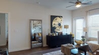 This single-floor residence offers a thoughtfully designed layout that balances comfort and modern style. The open-concept kitchen is a standout feature, equipped with stainless steel appliances including a gas range, built-in microwave, and refrigerator, all complemented by rich dark cabinetry, granite-style countertops, and a classic subway tile backsplash. A curved kitchen island with pendant lighting above provides additional seating and serves as a natural gathering point. Wood-style flooring runs throughout the main living areas, adding warmth and continuity to the space. The living room is bright and welcoming, featuring a ceiling fan, large artwork, and ample room for comfortable furnishings. A full-length mirror and dark credenza contribute to the room's refined aesthetic. The hallway connects to two well-sized bedrooms, each featuring ceiling fans, large windows that invite natural light, and dark wood-style flooring. Two bathrooms serve the residence — one with a tub-shower combination and warm-toned vanity cabinetry, and another featuring a glass-enclosed walk-in shower with clean white tile surround and granite vanity. The overall ambiance is modern and cohesive, with neutral tones and contemporary design elements throughout.