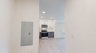 Located at 345 Lincoln Ave in Amherst, MA, this thoughtfully designed single-floor unit offers a clean, modern aesthetic throughout its well-appointed spaces. The open kitchen and dining area serves as a functional centerpiece, featuring two-tone cabinetry with white upper cabinets and dark lower cabinets, stainless steel appliances including a refrigerator, electric range, microwave, and dishwasher, complemented by white countertops and light wood-look flooring that flows seamlessly throughout the unit. Recessed lighting brightens the kitchen and dining space, which comfortably accommodates a dining table and chairs. The living room benefits from a large window framing lush, tree-lined views, creating a serene and naturally lit retreat. Two bedrooms each offer a compact, efficient layout with closet storage and windows that invite natural light. One bedroom provides direct access to a hallway leading to the bathroom. The unit includes two bathrooms, each finished with a floating wood-tone vanity, white countertop, large mirror, and light wood-look flooring. One bathroom features a combined shower and tub. A utility panel and storage are also conveniently accessible. The overall design is cohesive and contemporary, with a neutral palette and modern fixtures throughout.