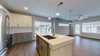 Located at 3125 Fire Ct in Charlotte, NC, this single-floor residence presents a thoughtfully designed open-concept layout with contemporary finishes throughout. The kitchen serves as a central focal point, showcasing a large island with a undermount sink, sleek white quartz countertops, and a two-tone cabinet scheme pairing white upper cabinets with sage-gray lower cabinets. A white subway tile backsplash complements the stainless steel appliances, including a refrigerator, range, and over-the-range microwave. Pendant lighting above the island adds a modern touch. The kitchen flows seamlessly into a spacious living area finished with rich wood-look flooring, multiple windows with blinds, and a ceiling fan, allowing generous natural light and views of the surrounding neighborhood. Bedrooms are carpeted for comfort, each featuring a ceiling fan and windows that bring in natural light. The bathrooms are well-appointed with gray shaker-style vanities, white quartz countertops, wood-look flooring, and tub-shower combinations with white tile surrounds. Ample built-in closet storage is also evident throughout, contributing to the home's practical and polished overall character.