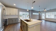 Located at 3125 Fire Ct in Charlotte, NC, this single-floor residence presents a thoughtfully designed open-concept layout with contemporary finishes throughout. The kitchen serves as a central focal point, showcasing a large island with a undermount sink, sleek white quartz countertops, and a two-tone cabinet scheme pairing white upper cabinets with sage-gray lower cabinets. A white subway tile backsplash complements the stainless steel appliances, including a refrigerator, range, and over-the-range microwave. Pendant lighting above the island adds a modern touch. The kitchen flows seamlessly into a spacious living area finished with rich wood-look flooring, multiple windows with blinds, and a ceiling fan, allowing generous natural light and views of the surrounding neighborhood. Bedrooms are carpeted for comfort, each featuring a ceiling fan and windows that bring in natural light. The bathrooms are well-appointed with gray shaker-style vanities, white quartz countertops, wood-look flooring, and tub-shower combinations with white tile surrounds. Ample built-in closet storage is also evident throughout, contributing to the home's practical and polished overall character.