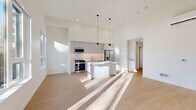 This thoughtfully designed single-floor residence offers a clean, modern aesthetic throughout its well-appointed layout. The open-concept kitchen and living area serves as the heart of the home, boasting soaring ceilings that amplify the sense of space. The kitchen is outfitted with sleek gray shaker-style cabinetry, a herringbone tile backsplash, stainless steel appliances including a gas range and French door refrigerator, and a white waterfall-edge island illuminated by stylish cone pendant lights. Light pours in through large windows and a glass door in the living area, which opens to an outdoor balcony with tree-lined views. Light-toned hardwood flooring flows seamlessly throughout the space, enhancing the bright, airy atmosphere. A clean hallway connects the main living area to the private bedroom, which features a wide horizontal window with outdoor views and a sliding-door closet. The full bathroom is finished with large-format gray tile surrounding a soaking tub and shower combo, a white vanity with an undermount sink, and a full-width mirror. A dedicated laundry room with a side-by-side front-load washer and dryer completes this efficient, contemporary home.