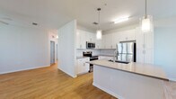 Located at 6134 Willow Beck Ln in Bradenton, Florida, this single-story residence presents a clean, contemporary design throughout its well-appointed layout. The open-concept kitchen serves as a central highlight, showcasing white shaker cabinetry, a classic subway tile backsplash, stainless steel appliances including a refrigerator, microwave, and range, and a spacious center island with a dark contrasting countertop and integrated sink. Pendant lighting above the island adds a polished finishing touch. The kitchen flows seamlessly into the living and dining areas, which are finished with warm hardwood-style flooring and neutral white walls that promote a bright, airy atmosphere. Multiple windows allow natural light to fill the living space. The bedroom features plush carpeting and a window with exterior views. The bathroom is outfitted with a wood-toned vanity, white countertop, large mirror, and a tiled tub-shower combination. A dedicated laundry room houses a full-size washer and dryer with overhead shelving for additional storage. The attached garage offers a concrete floor and automatic door opener, providing practical covered parking and extra storage capacity.