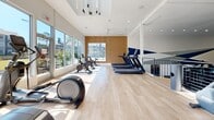 Located in Atlanta, GA, this two-floor fitness facility offers a comprehensive and thoughtfully designed exercise environment. The ground floor greets visitors with an open, airy layout featuring light hardwood flooring, soaring double-height ceilings, and abundant natural light streaming through floor-to-ceiling windows that frame views of the surrounding community's lush greenery. This level houses a generous cardio zone lined with treadmills, ellipticals, and cycling bikes, as well as an open studio area with hardwood floors ideal for stretching or group workouts. A striking rock climbing wall adds a distinctive athletic element to the space.

A sculptural spiral staircase connects to the upper floor, which expands the facility's strength training offerings. The second level features rubber flooring throughout, an extensive array of weight machines, free weights, benches, and functional training equipment, including a turf lane equipped with a sled for performance training. Bold navy and white geometric murals punctuate the walls alongside a dynamic athlete sketch, lending a motivating, energetic ambiance. A warm wood-slatted partition adds an architectural accent, while large mirrors and recessed lighting enhance the sense of space. A mezzanine overlook connects both levels visually, reinforcing the facility's impressive scale and cohesive design.