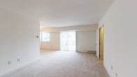 This single-floor residence offers a clean, neutral aesthetic throughout, with soft beige carpeting and crisp white walls creating a bright and versatile living environment. The open living area is generously proportioned, featuring large sliding glass doors dressed with vertical blinds that allow abundant natural light to fill the space. A ceiling fan adds practical comfort to the adjoining area, which flows seamlessly between rooms.

The kitchen is outfitted with warm honey-toned cabinetry, dark granite-style countertops, and a tasteful stone tile backsplash. A full suite of black Whirlpool appliances — including a range, dishwasher, microwave, and refrigerator — provides complete functionality, all set atop durable tile flooring.

The bedrooms are well-sized and carpeted, with natural light provided by horizontal-blind windows. The primary bedroom stands out with a notable dual closet configuration, offering substantial built-in storage. Additional rooms also feature closet access.

Two bathrooms serve the residence. One includes a clean white soaking tub with a tiled surround, while the other presents a warm wood-toned vanity with a white countertop, chrome fixtures, and crisp tile flooring. The overall layout, as seen in the dollhouse view, is efficiently organized and easy to navigate.