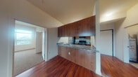 Located on the fourth floor at 300 E 13th St in Vancouver, Washington, Unit 407 is a thoughtfully designed residential unit offering a clean, modern aesthetic throughout. Rich, dark hardwood flooring flows through the main living and kitchen areas, creating a warm and inviting atmosphere. The open-concept kitchen is anchored by a peninsula with granite countertops, providing both prep space and a casual dining area. Warm wood cabinetry extends to the ceiling, offering generous storage, while stainless steel appliances — including a refrigerator, range, and microwave — complete the functional workspace. The spacious living area is filled with natural light from multiple windows and a glass door that leads to an outdoor balcony, offering views of the surrounding Vancouver cityscape. The bedroom features plush carpeting and a large window that continues to bring in abundant natural light and outdoor views. Two bathrooms serve the unit: one with a full tub-and-shower combination with tile surround, granite vanity, and wood cabinetry, and a second with a granite-topped vanity and tile flooring. The unit's neutral color palette and consistent finishes throughout create a cohesive and comfortable living environment well suited for everyday living.