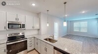 Located on Louis Stephens Drive in Durham, NC, this well-appointed 2-bedroom, 3-bathroom residence offers a thoughtfully designed single-floor layout. The open-concept kitchen is a standout feature, showcasing granite countertops, white shaker-style cabinetry, stainless steel appliances including a French door refrigerator, electric range, and microwave, as well as a peninsula with pendant lighting that flows seamlessly into the living area. Wood-style flooring runs throughout the home, adding warmth and continuity across every room. The living room is bright and airy, benefiting from large windows with blinds and a glass-paneled exterior door that invites natural light. The primary bedroom is generously sized, complete with a ceiling fan, dedicated closet space, and an en-suite bathroom featuring a granite vanity, large mirror, and a shower-tub combination. The second bedroom mirrors this comfortable scale, also equipped with a ceiling fan and its own closet. Each of the three bathrooms maintains consistent finishes, including granite countertops and clean white fixtures. Neutral gray walls and crisp white trim create a modern, cohesive aesthetic throughout the space, making it move-in ready and highly versatile.