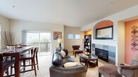 This two-story home offers a thoughtfully designed layout with 2 bedrooms, 3 bathrooms, and a dedicated office spread across two well-proportioned floors. The main level features an open-concept living, dining, and kitchen area filled with natural light. The living room is anchored by a tile-surround fireplace framed by a warm orange accent wall with an elegant arched niche, complemented by built-in shelving. Sliding glass doors lead to an outdoor balcony with views of surrounding greenery. The dining area benefits from an expansive picture window that bathes the space in natural light. The kitchen is outfitted with light maple cabinetry, granite countertops, stainless steel appliances, and recessed lighting. Carpeted stairs with a handrail connect the two floors. Upstairs, the primary bedroom features vaulted ceilings and a soft blue accent wall, creating a calm and airy retreat. The office stands out with bold red walls, vaulted ceilings, and a bright window. The bathrooms are well-appointed, with one featuring warm green walls, tile flooring, and stone-topped vanities. Throughout the home, neutral tones, carpet flooring, and consistent trim work provide a cohesive and inviting atmosphere.