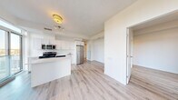 This efficiently designed 2-bedroom, 2-bathroom unit offers a thoughtful layout across a single floor. The open-concept kitchen and living area serves as the heart of the space, featuring light hardwood-style flooring that extends throughout. The kitchen is equipped with stainless steel appliances including a refrigerator, electric range, built-in microwave, and dishwasher, all complemented by crisp white cabinetry, clean white countertops, and a tile backsplash. A functional breakfast bar provides a seamless transition into the living area. Both bedrooms are bright and airy, each benefiting from large floor-to-ceiling windows that invite generous natural light and offer open views of the surrounding urban landscape with tree-lined streetscapes. The two bathrooms are finished in a clean, modern style with white vanities and tile flooring. A dedicated in-unit stacked washer and dryer adds everyday convenience. The hallways connect the rooms with ease, and the overall palette of whites and light neutrals throughout gives the space a fresh, contemporary feel. The unit also features a distinctive structural column in the living area, adding an architectural character to the interior.