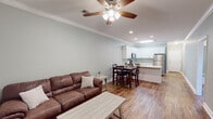 This single-story space in Valdosta, Georgia, is designed with a clean, modern aesthetic highlighted by soft sage-green walls, crisp white trim, and warm hardwood-style flooring that runs throughout the main living areas. Crown molding and recessed lighting add a polished touch, while ceiling fans in each room ensure year-round comfort.

The open-concept living area flows seamlessly into the kitchen and dining space, creating an inviting, connected layout. The kitchen is well-equipped with white shaker-style cabinetry, granite countertops, stainless steel appliances including a refrigerator, microwave, and range, and a peninsula that doubles as additional prep and seating space. A dining table with high-back chairs sits adjacent, completing the functional eat-in arrangement.

Two bedrooms offer comfortable, carpeted retreats, each featuring a ceiling fan with light fixture and a window that allows natural light to filter in. The full bathroom includes a tub-shower combination, white vanity with granite countertop, and hardwood-style flooring. A dedicated laundry area accommodates a full-sized washer and dryer, adding everyday convenience to this thoughtfully designed space.