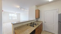 This single-floor, one-bedroom, one-bathroom unit offers a functional and well-appointed layout designed for comfortable everyday living. The open-concept design connects the kitchen and living area seamlessly, creating a spacious and airy feel throughout the main living space. Track lighting overhead and a ceiling fan contribute to a bright, well-lit environment, while a large window in the living area allows natural light to fill the room. Flooring transitions from tile in the entry and kitchen to plush carpet in the living and bedroom areas.

The kitchen is efficiently designed with warm wood cabinetry, granite-style countertops, and a double-basin stainless steel sink. A peninsula counter separates the kitchen from the living area, providing additional workspace. Black appliances—including a refrigerator, electric range, over-the-range microwave, and dishwasher—complete the kitchen. A louvered pantry door provides convenient storage.

The bedroom is a well-proportioned, carpeted space featuring a ceiling fan, a window with natural light and outdoor views, and easy access to a closet.

The bathroom includes a single-vanity with wood cabinetry, a white countertop, tile flooring, and a soaking tub with shower combination, finished with brushed nickel hardware throughout.