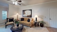 This single-floor residence offers a thoughtfully designed layout that maximizes functionality and comfort throughout its key living spaces. The living room serves as the central gathering area, featuring plush carpeting, a tray ceiling with a ceiling fan, and neutral-toned walls that create a bright, welcoming atmosphere. The kitchen is equipped with warm wood cabinetry, tile flooring, black appliances including a full-size refrigerator and dishwasher, and a double sink beneath a window that allows natural light to filter in. A breakfast bar connects the kitchen to the adjacent dining area, which accommodates a round table and chairs alongside a decorative wall-mounted panel and framed artwork. The bedroom is generously sized with soft carpeting, a large window dressed with sheer curtains, a closet, and neutral walls that contribute to a calm, restful environment. The full bathroom features tile flooring, a wide vanity with warm wood cabinetry, a large mirror with overhead lighting, and a shower-tub combination. Crown molding and consistent finishes throughout the space tie the interior together with a cohesive, polished aesthetic.