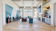 Located at 7550 S Blackhawk St in Englewood, Colorado, this single-floor clubhouse lobby for Dove Valley Apartments delivers an impressive first impression through refined architectural design and upscale finishes. The entrance features a grand arched transom window above sleek black-framed double doors, opening into a wide hallway flanked by glass-paneled rooms that guide visitors toward the main gathering space.

The central lounge area is defined by soaring ceilings with elegant coffered and tray detailing, complemented by a striking modern chandelier. Light hardwood flooring runs throughout, adding warmth to the bright, airy interior. A dramatic curved wall of floor-to-ceiling windows floods the space with natural light and offers outdoor views, while a dedicated seating nook with a round dining table provides an inviting area to relax.

A bold geometric teal accent wall serves as a focal point, enhancing the contemporary aesthetic. The lounge is furnished with plush teal armchairs, a tufted sofa, and a gold coffee table arranged atop a textured area rug. On the opposite side, a classic white fireplace mantle anchors a cozy seating arrangement, accompanied by a built-in refreshment station with shelving and a beverage cooler. The overall ambiance is polished, welcoming, and thoughtfully designed for community living.