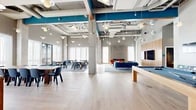 Located at 222 Canal St in New Haven, CT, this expansive single-floor amenity space offers a generously sized, open-plan layout designed for both socializing and relaxation. The interior showcases an industrial-modern aesthetic, with soaring exposed ceilings highlighted by bold teal beams, visible ductwork, and an eclectic array of pendant lighting that adds warmth and character throughout.

Light hardwood flooring runs continuously across the space, tying together three distinct functional zones. A dining and collaboration area near the floor-to-ceiling windows features round wooden tables and navy blue chairs arranged on textured area rugs, bathed in abundant natural light with street-level views of the New Haven neighborhood. A central lounge zone anchors the space with a teal sofa, colorful accent pillows, and a wood-paneled feature wall with a mounted flat-screen TV. Nearby, two vibrant orange swivel chairs flank a striking gold-framed fireplace with a perforated metallic surround, creating an intimate and stylish retreat. A recreation area rounds out the space with a full-size billiard table and bench seating. A built-in kitchenette with light wood cabinetry, white upper cabinets, and an additional mounted TV provides a functional service hub. Exposed concrete columns throughout reinforce the building's industrial heritage while complementing the contemporary furnishings.