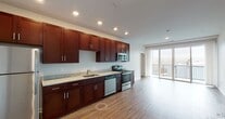 This single-floor residence offers a thoughtfully designed layout with modern finishes throughout. The kitchen serves as a functional centerpiece, showcasing rich dark mahogany-toned cabinetry that extends to the ceiling, providing generous storage. Light granite countertops complement the cabinetry, while a full suite of stainless steel appliances — including a refrigerator, electric range, over-the-range microwave, and dishwasher — equips the space for everyday living. Recessed lighting illuminates the kitchen and adjacent living area, which features warm hardwood-style flooring that carries throughout the unit. A sliding glass door opens to a private balcony, bringing in natural light and outdoor views. The bedrooms are well-proportioned, finished with the same durable hardwood-style flooring and neutral wall tones, each benefiting from natural light through sizable windows. One bedroom features direct access to a bathroom. The bathrooms are clean and classic in design, featuring white subway tile tub-and-shower surrounds, chrome fixtures, dark wood vanities with light countertops, and tile flooring. The overall aesthetic is modern and cohesive, combining practical finishes with a bright, neutral palette throughout.