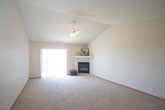 This well-maintained single-floor home offers a thoughtfully designed layout that balances comfort and functionality. The expansive living room is the heart of the space, highlighted by soaring vaulted ceilings and a ceiling fan that enhances the sense of openness. A corner fireplace with a clean white mantle serves as a natural focal point, while a large sliding glass door floods the room with natural light and provides access to the outdoors. A pass-through window connects the living area to the kitchen, maintaining an open, airy feel throughout.

The galley-style kitchen is efficiently arranged with ample white cabinetry on both sides, generous countertop space with neutral-toned laminate surfaces, and patterned tile flooring. White appliances complete the clean, classic look.

The bedrooms are carpeted and generously sized, each featuring neutral walls and vertical blinds that allow for natural light while maintaining privacy. One bedroom includes multiple doorways, suggesting access to a closet and additional spaces.

The bathroom is finished with patterned tile flooring, a single-sink vanity with white cabinetry, a large mirror, and a shower-tub combination. Throughout the home, warm wood baseboards, soft neutral tones, and plush carpeting create a welcoming and cohesive atmosphere.