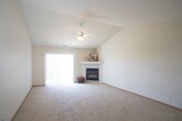 This well-maintained single-floor home offers a thoughtfully designed layout that balances comfort and functionality. The expansive living room is the heart of the space, highlighted by soaring vaulted ceilings and a ceiling fan that enhances the sense of openness. A corner fireplace with a clean white mantle serves as a natural focal point, while a large sliding glass door floods the room with natural light and provides access to the outdoors. A pass-through window connects the living area to the kitchen, maintaining an open, airy feel throughout.

The galley-style kitchen is efficiently arranged with ample white cabinetry on both sides, generous countertop space with neutral-toned laminate surfaces, and patterned tile flooring. White appliances complete the clean, classic look.

The bedrooms are carpeted and generously sized, each featuring neutral walls and vertical blinds that allow for natural light while maintaining privacy. One bedroom includes multiple doorways, suggesting access to a closet and additional spaces.

The bathroom is finished with patterned tile flooring, a single-sink vanity with white cabinetry, a large mirror, and a shower-tub combination. Throughout the home, warm wood baseboards, soft neutral tones, and plush carpeting create a welcoming and cohesive atmosphere.